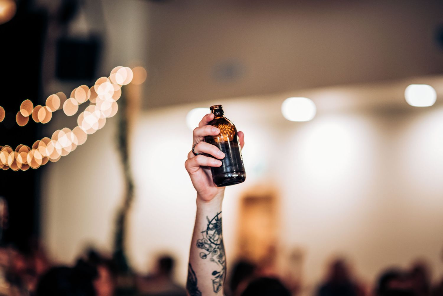 Tattooed arm holding up a dark bottle at celebration event.