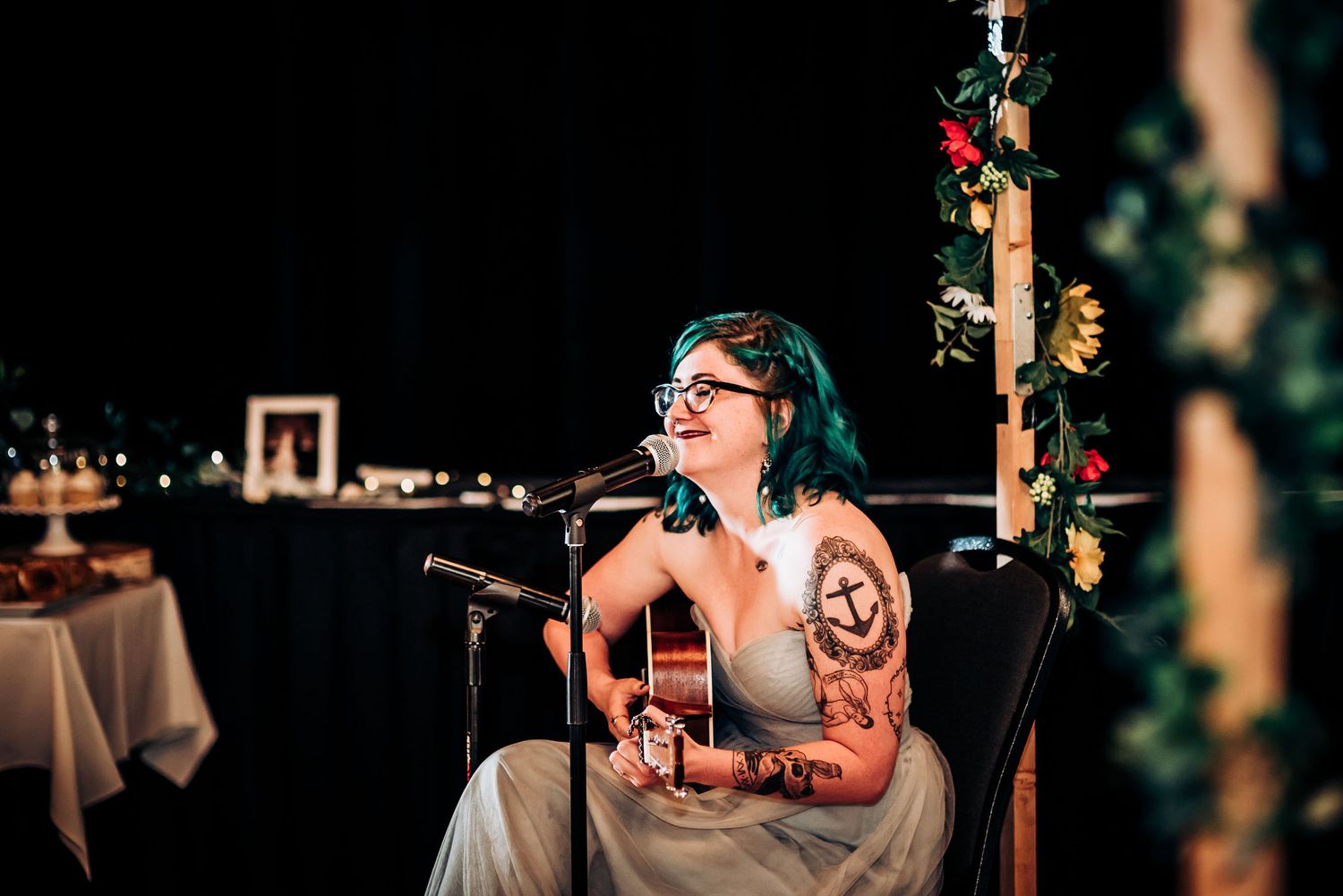 Performer with colorful hair plays acoustic guitar during intimate wedding reception.