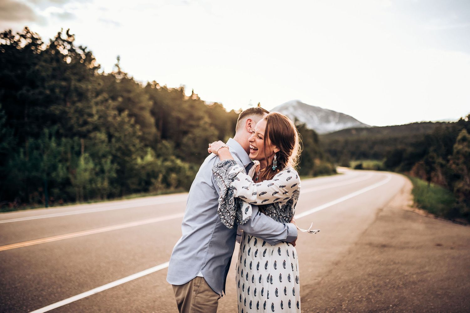 Couple sharing romantic embrace on scenic mountain road at sunset.
