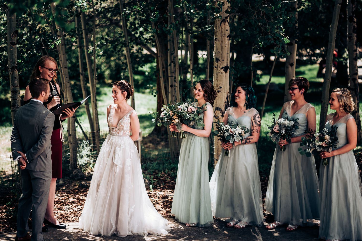 An outdoor forest wedding ceremony with bridesmaids in soft pastel dresses standing in line.
