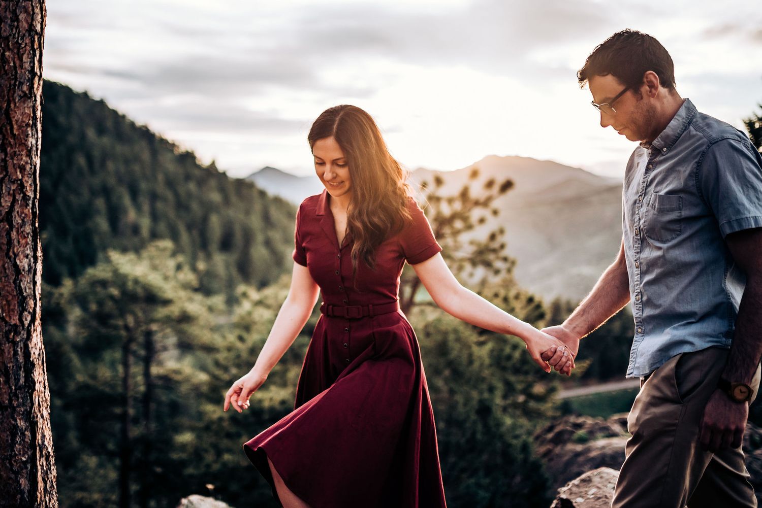 Wind catches woman's burgundy dress as couple shares moment on mountain trail.