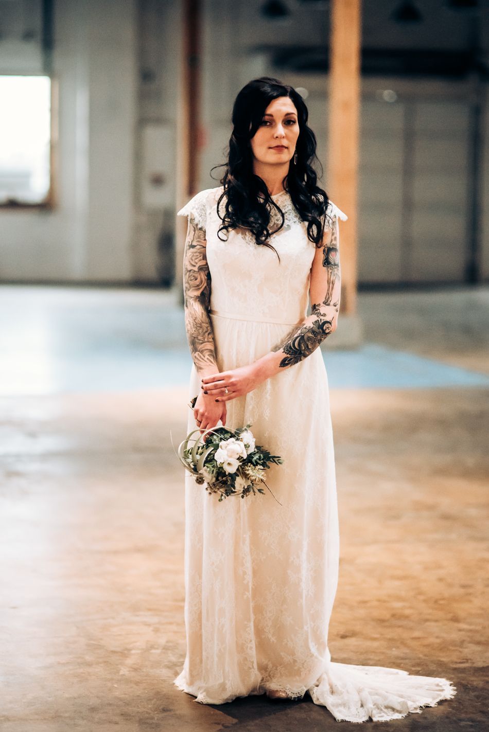 Full-length portrait of bride in lace gown holding white bouquet.