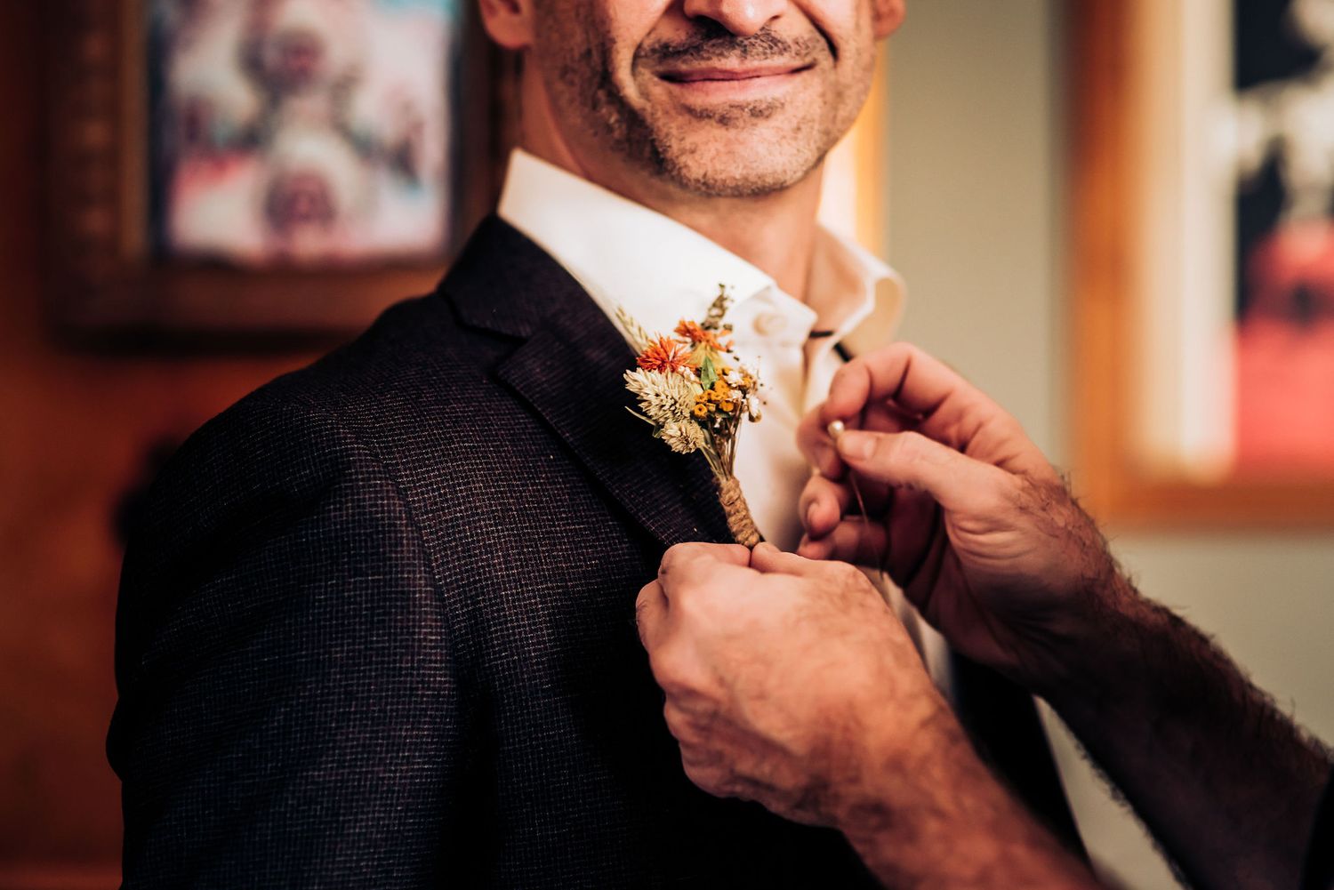 Close-up of groom adjusting floral boutonniere on dark suit jacket.