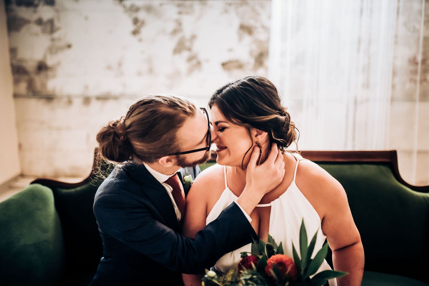Romantic wedding moment captured on a vintage green velvet couch in a minimalist setting.