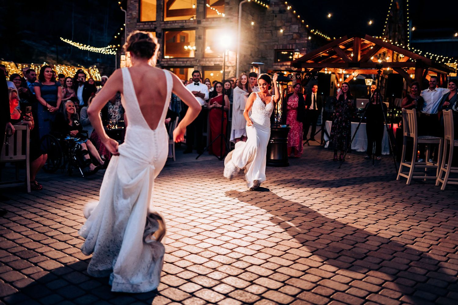 A nighttime wedding dance on a brick patio with string lights and onlooking guests.
