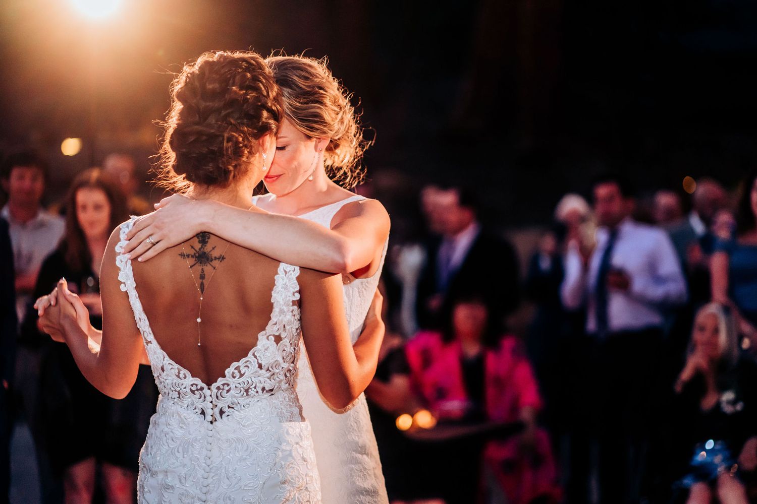 A romantic first dance moment between newlyweds wearing white dresses under warm lighting.