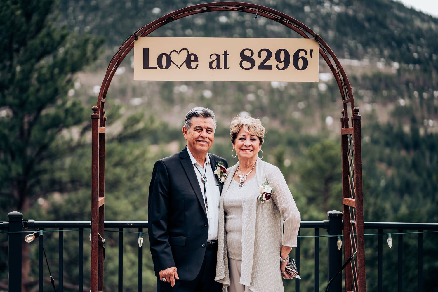 A couple stands under an arched 'Love at 8296' sign with mountain backdrop at their outdoor wedding.