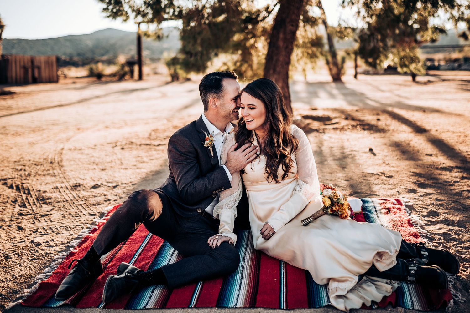 A couple shares a tender moment on a striped picnic blanket during an outdoor photoshoot.