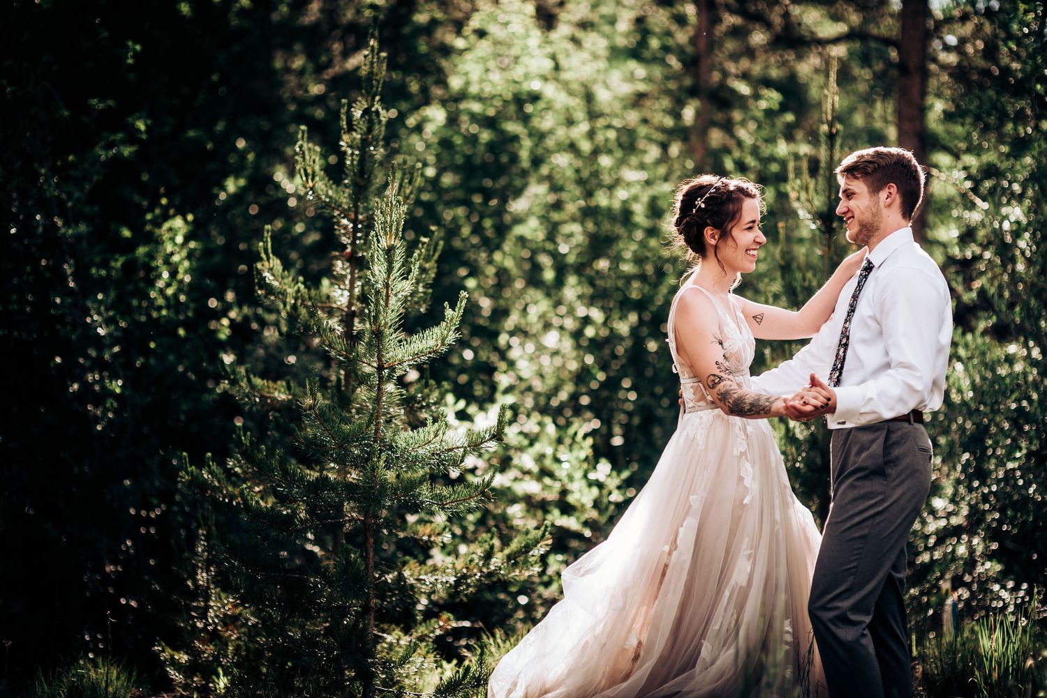 A romantic forest wedding portrait with sunlight streaming through the trees behind the couple.