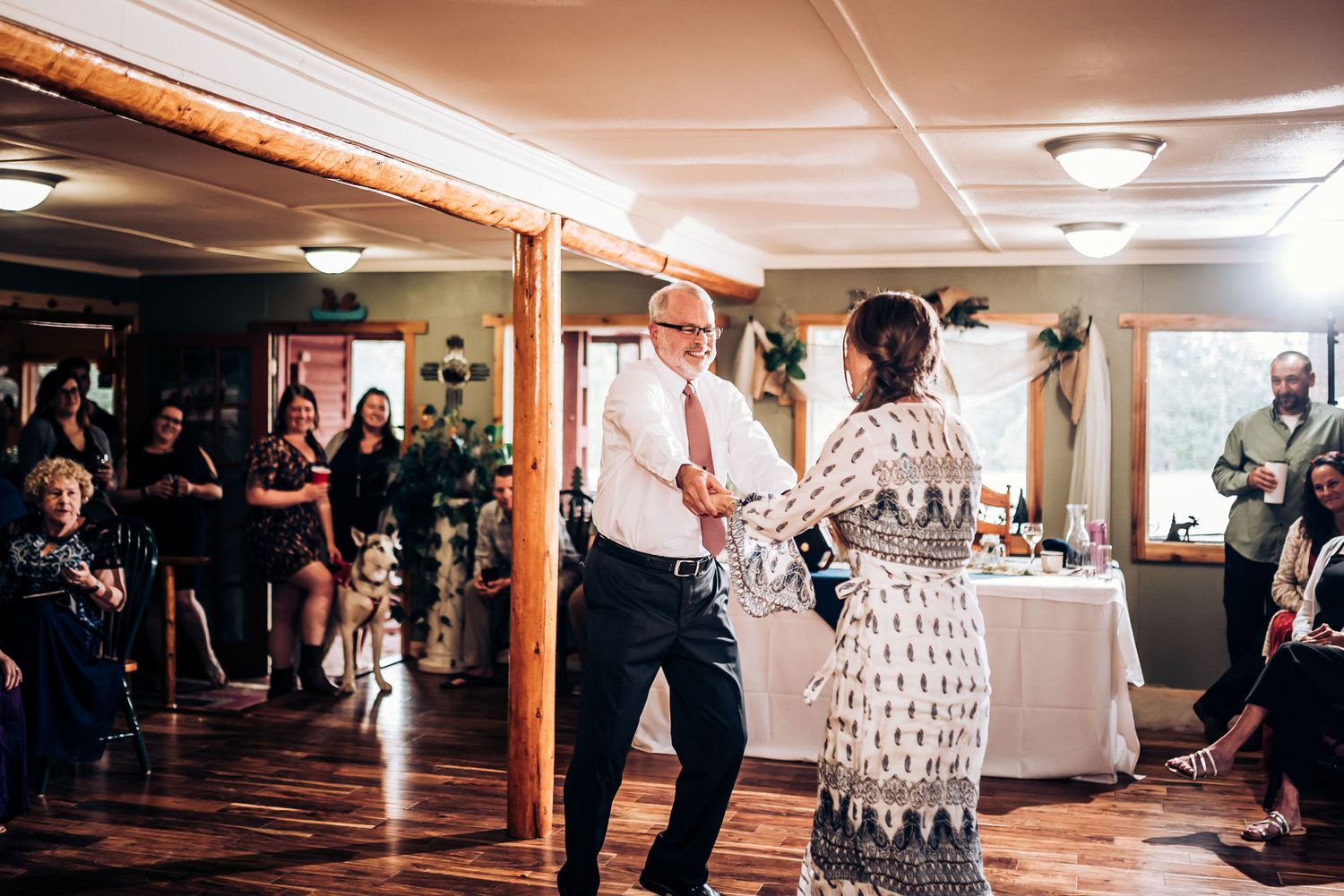 Older gentleman and woman dance joyfully at a wedding reception as guests look on.