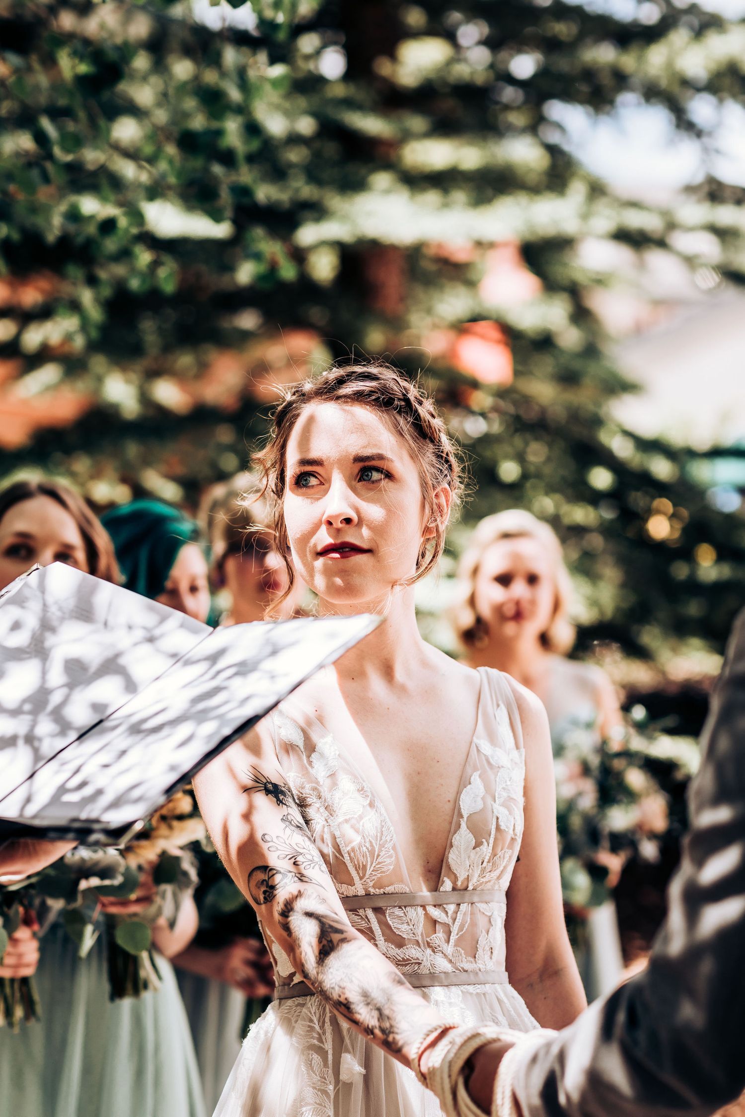 A bride in a plunging v-neck wedding gown listens intently during an outdoor ceremony.