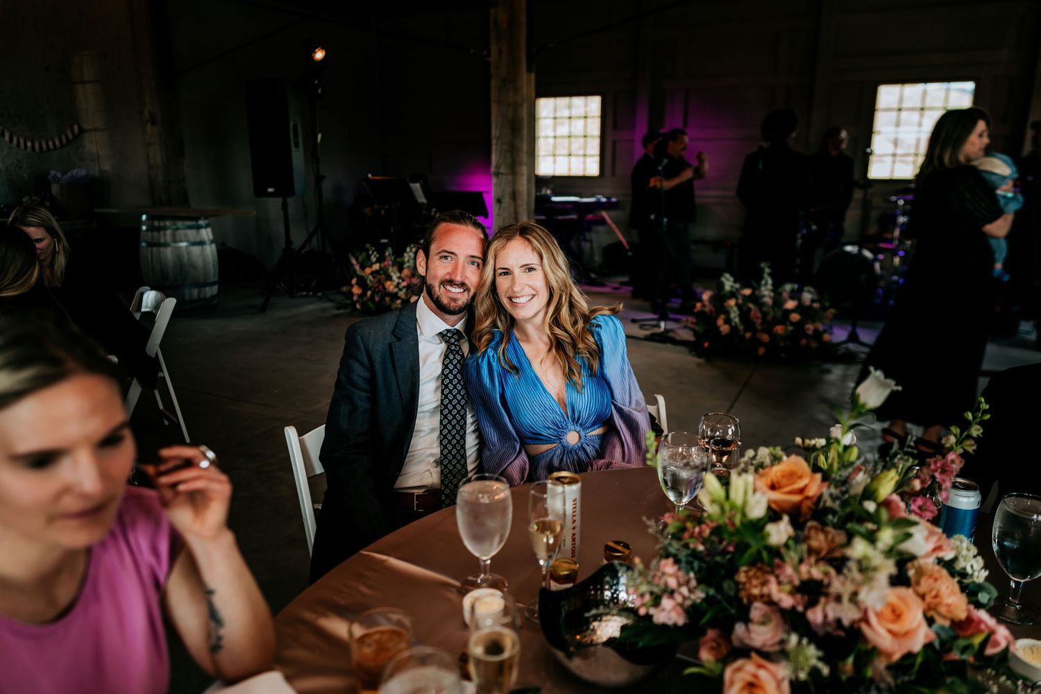 Guests seated at a wedding reception table with vibrant floral arrangements and wine glasses.