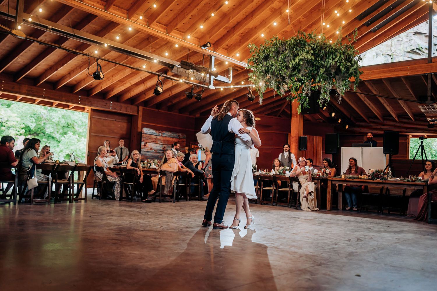 Couple shares an intimate dance moment under wooden beams and string lights.