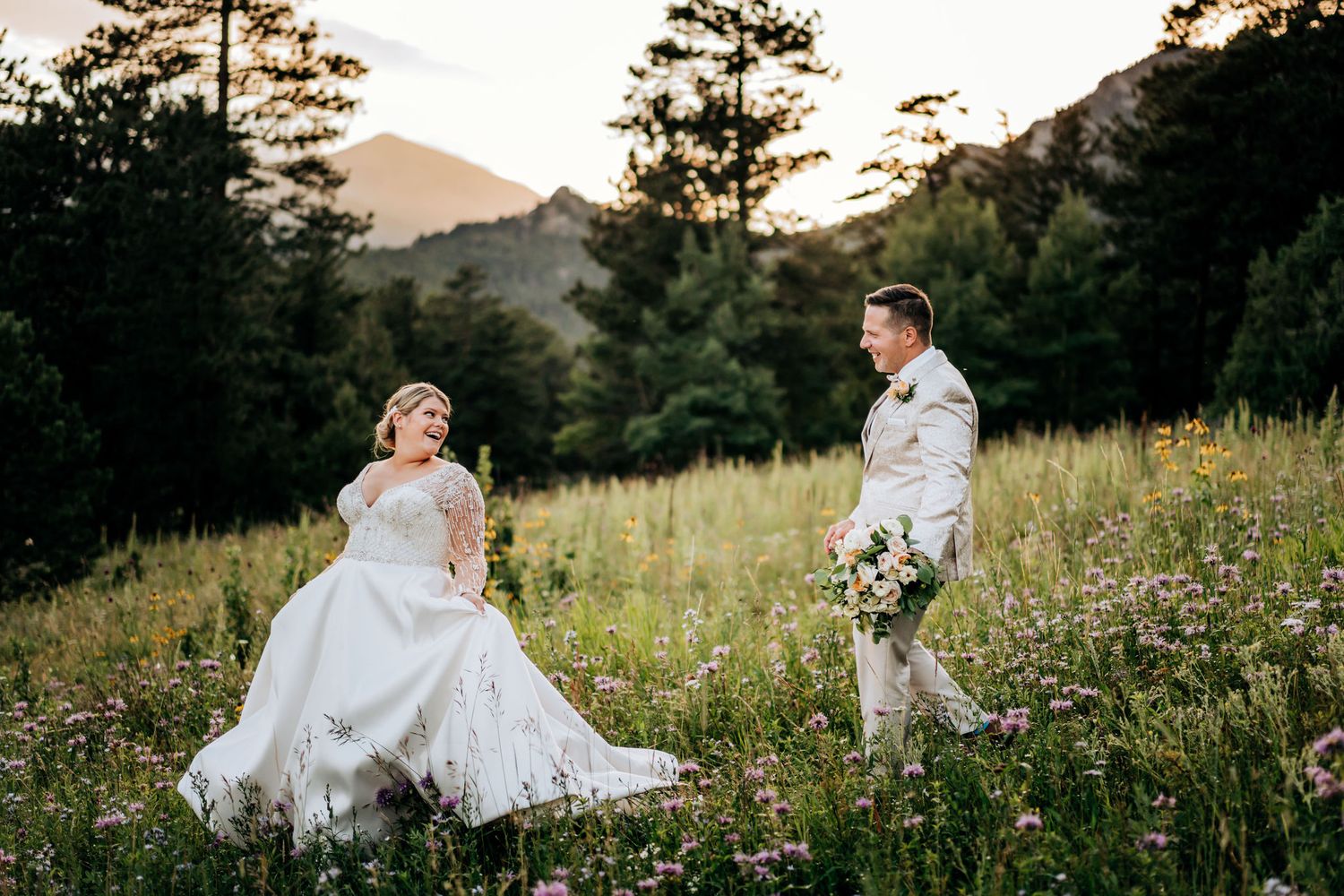 Wedding couple in mountain meadow with wildflowers at sunset.