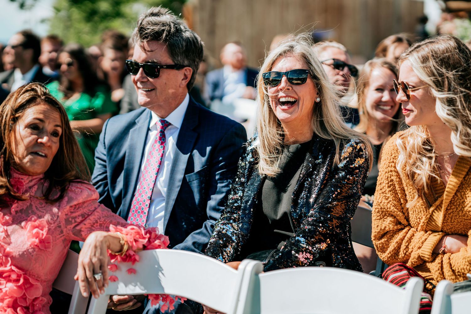 Wedding attendees in colorful attire share joyful laughter during an outdoor celebration.