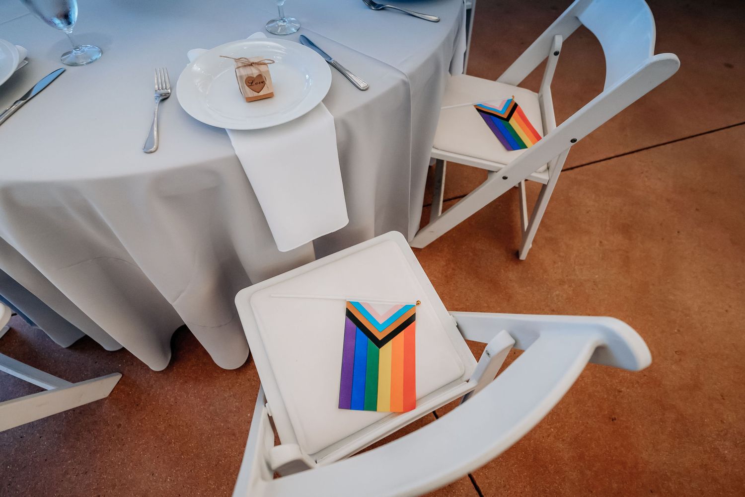 Table setting with rainbow pride flags and white linens at a wedding reception.