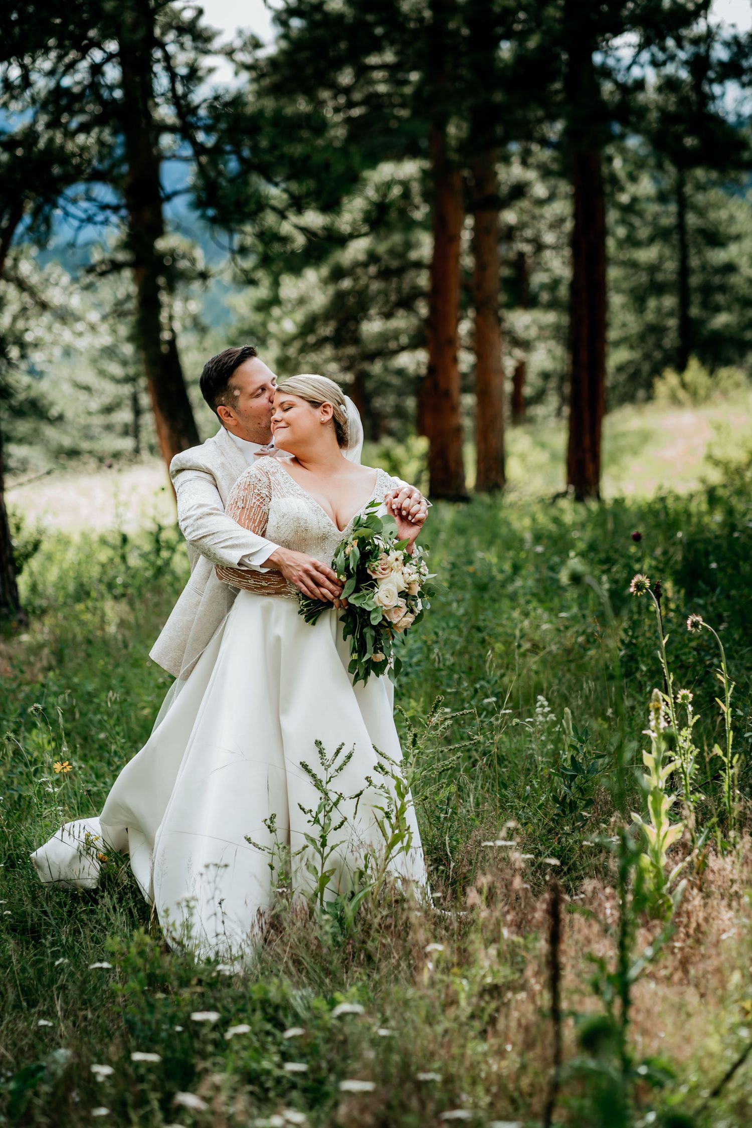 Intimate wedding moment captured in a pine forest with wildflowers and natural lighting.