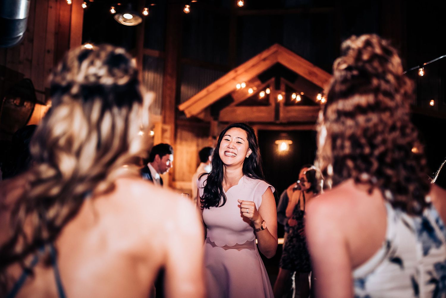 Reception guests enjoy lively conversation and dancing in warmly lit rustic venue.