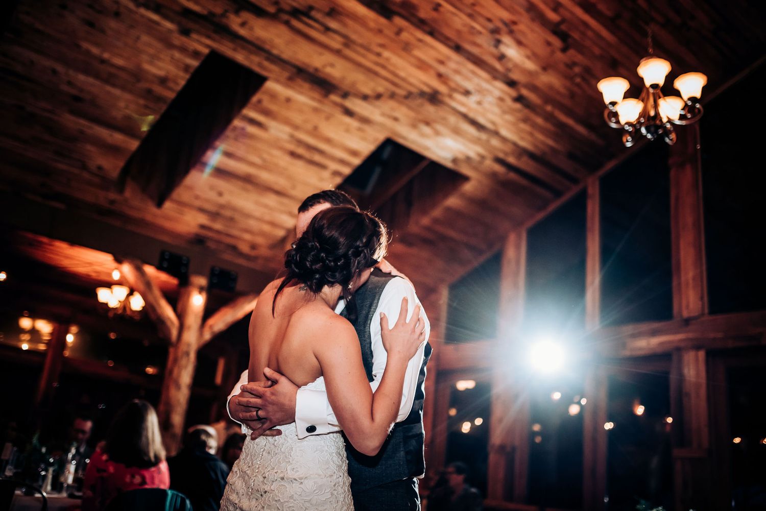 Couple shares their first dance in a rustic barn venue with wooden beams and warm lighting.