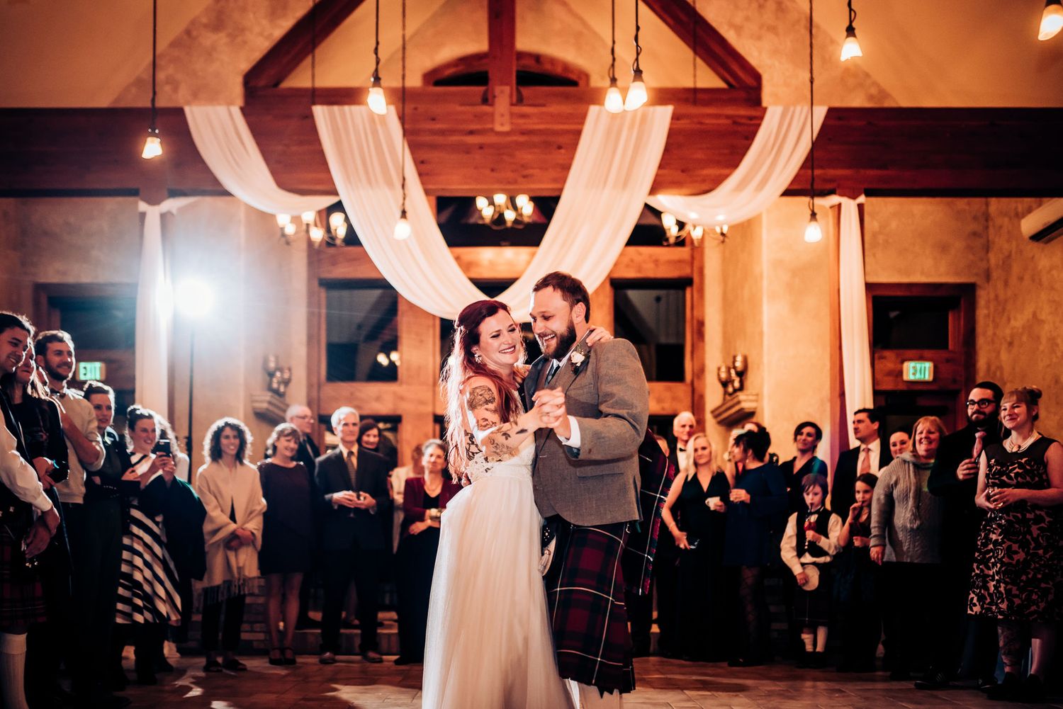Newlyweds share dance under rustic wooden beams and elegant white draping.