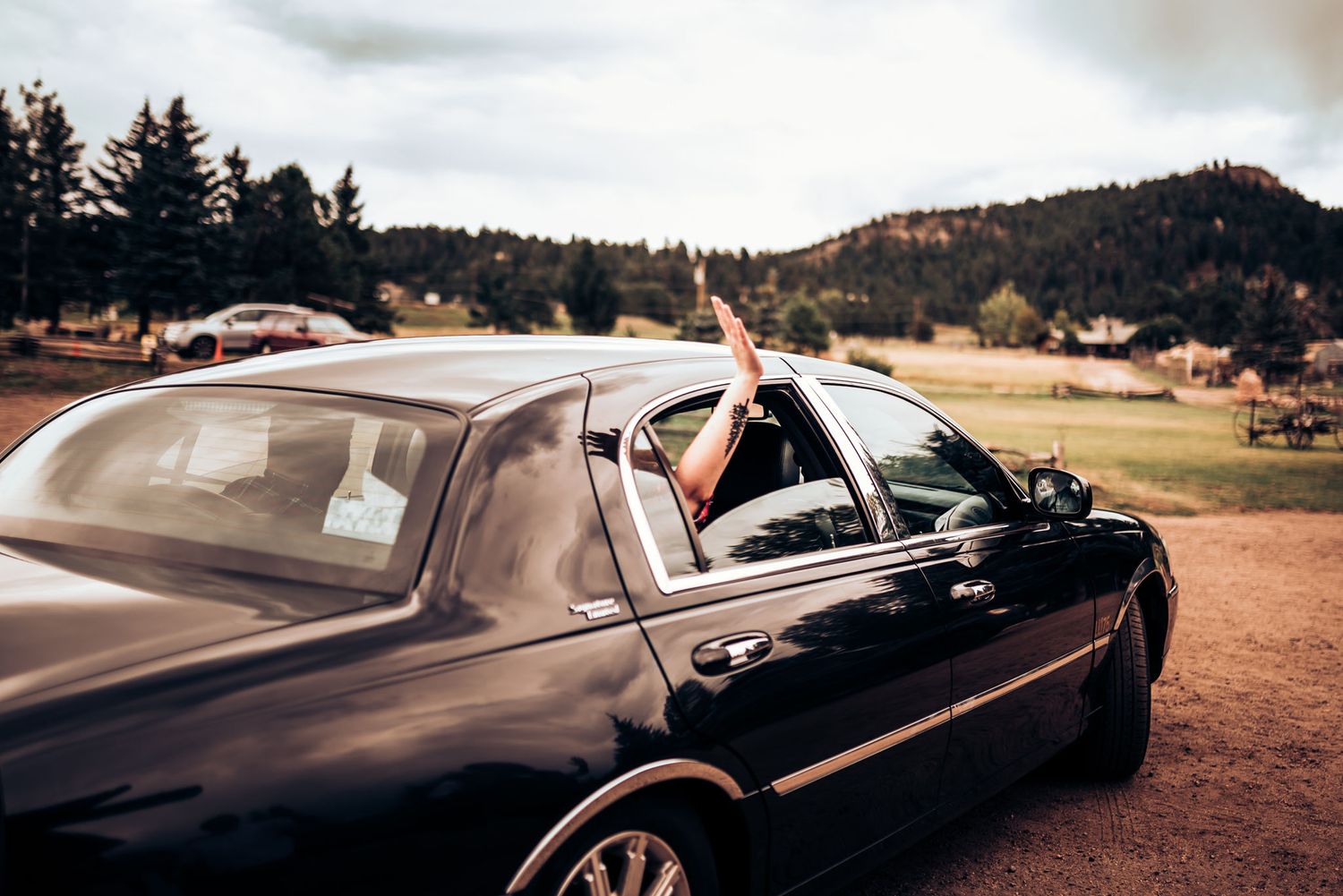 Luxury black car parked in mountainous landscape with arm waving from window.
