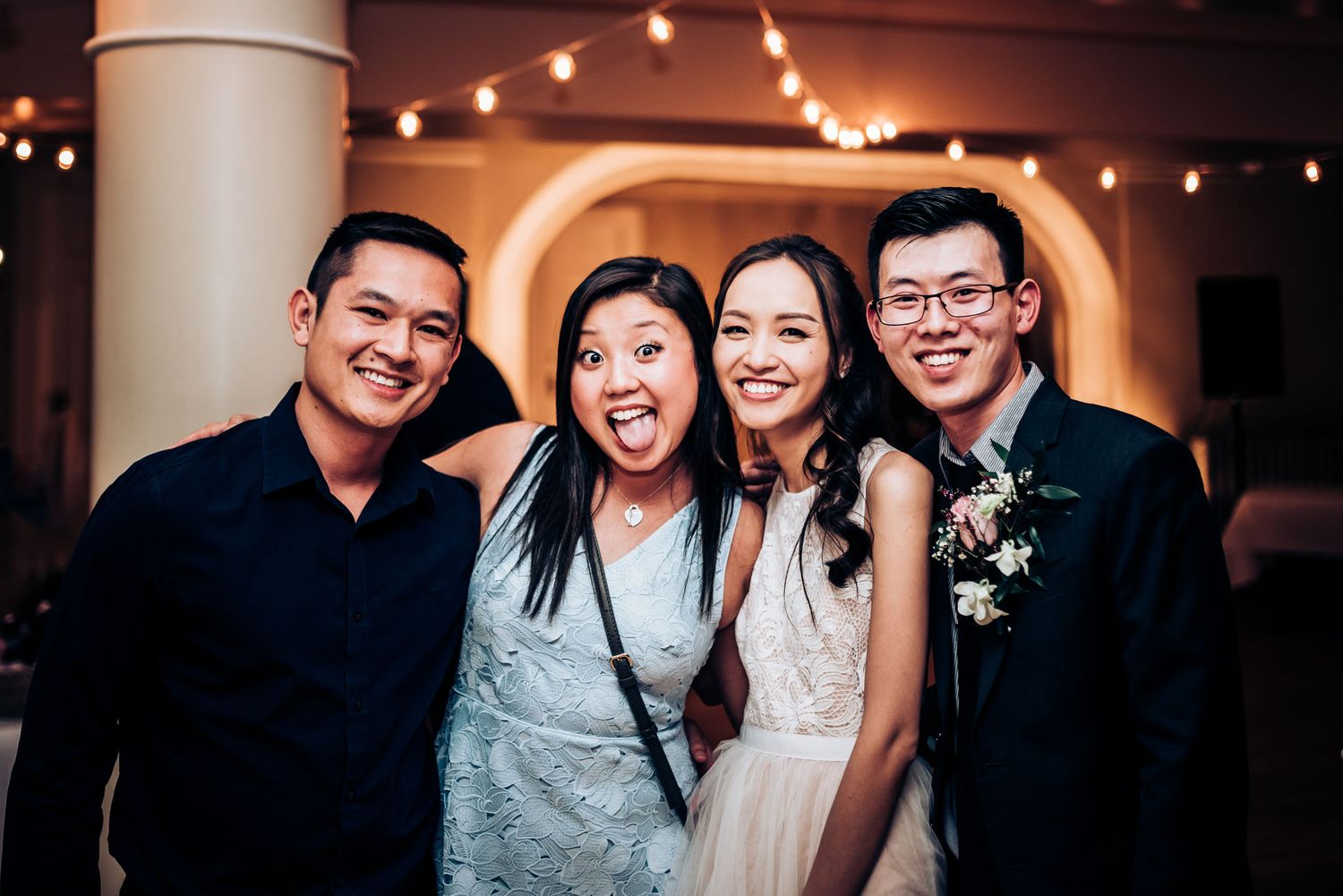 A group poses together during a wedding celebration with string lights in the background.