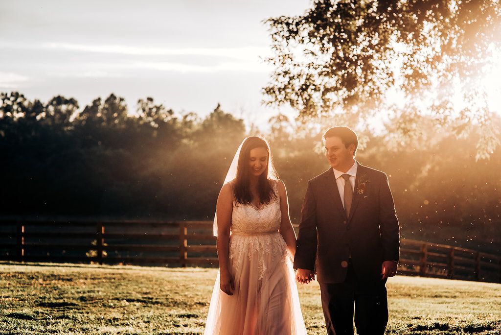 Couple walking through sunlit field during golden hour wedding photos.