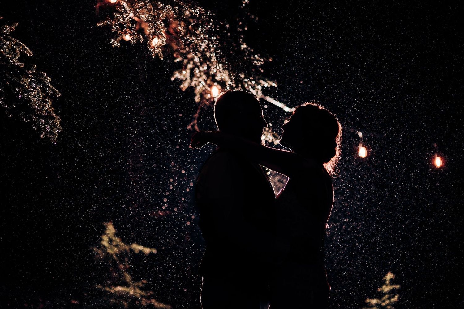 Romantic silhouette of couple dancing under string lights and night sky.