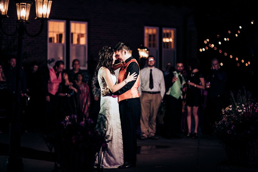 Romantic first dance under ambient lighting at an outdoor evening wedding reception.