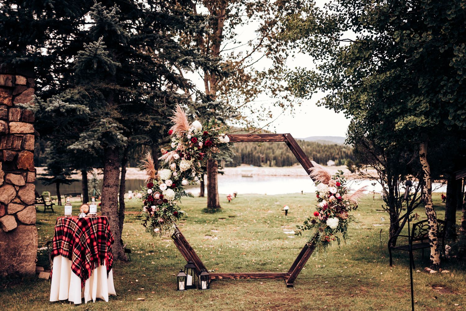 Outdoor wedding ceremony setup with floral arch and plaid accents in natural setting.