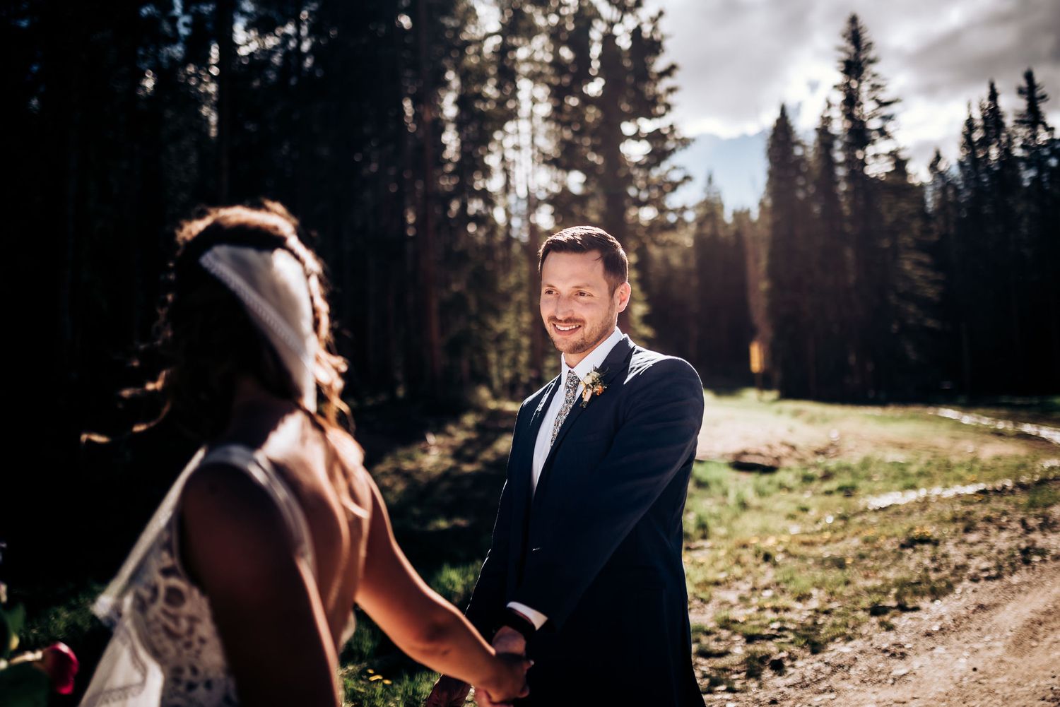 Outdoor mountain wedding ceremony with sunlight filtering through forest trees.