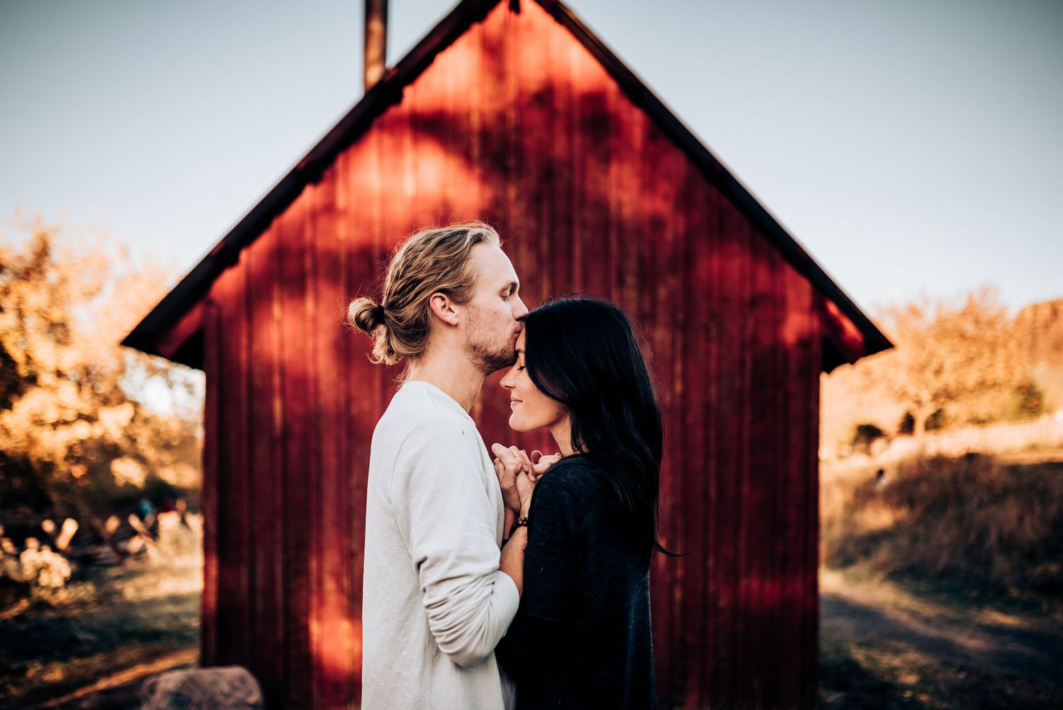 A romantic moment shared between a couple in front of a red barn during golden hour.