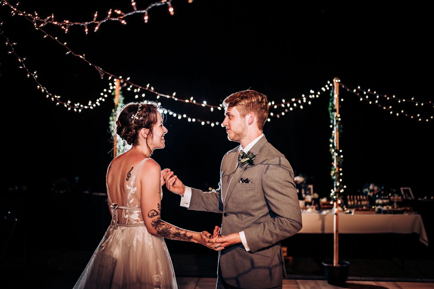 Couple dancing beneath romantic string lights during evening reception celebration.