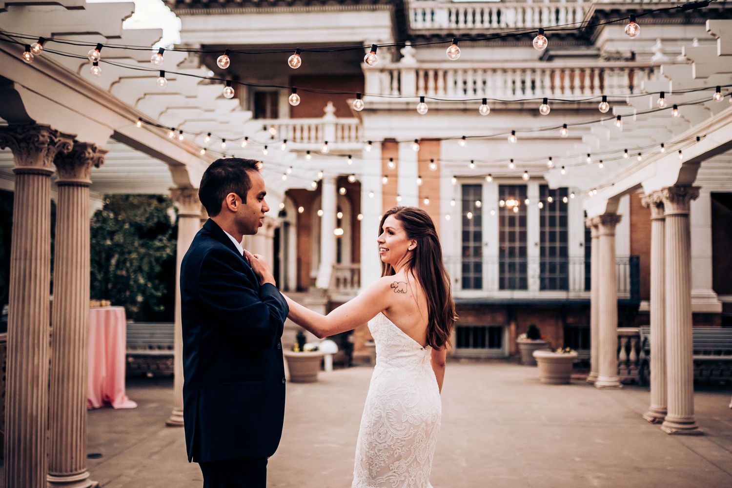 A couple dances together under twinkling lights in a classic columned courtyard.