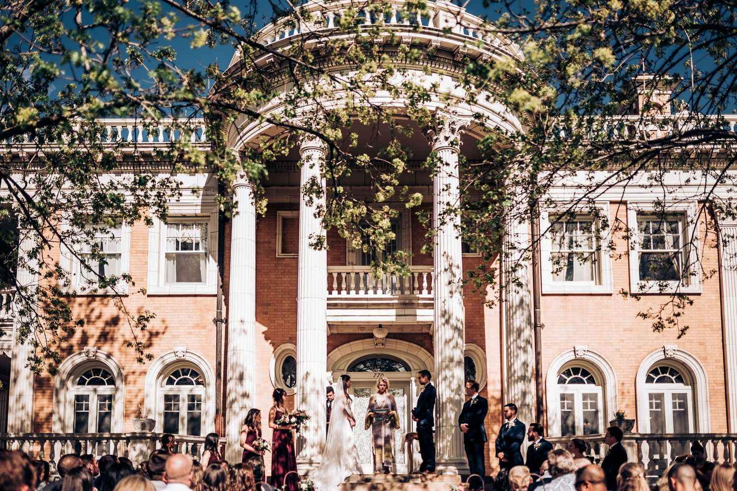 Wedding ceremony in front of a beautiful pink mansion with Greek revival architecture.