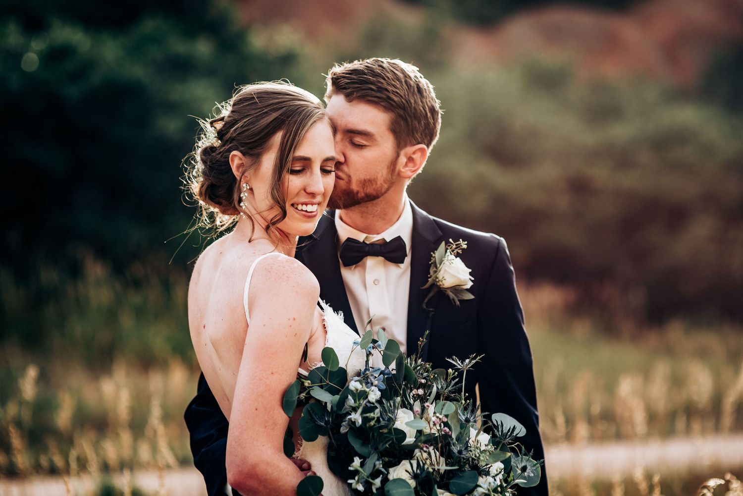 Intimate wedding portrait with couple and eucalyptus bouquet against nature backdrop.
