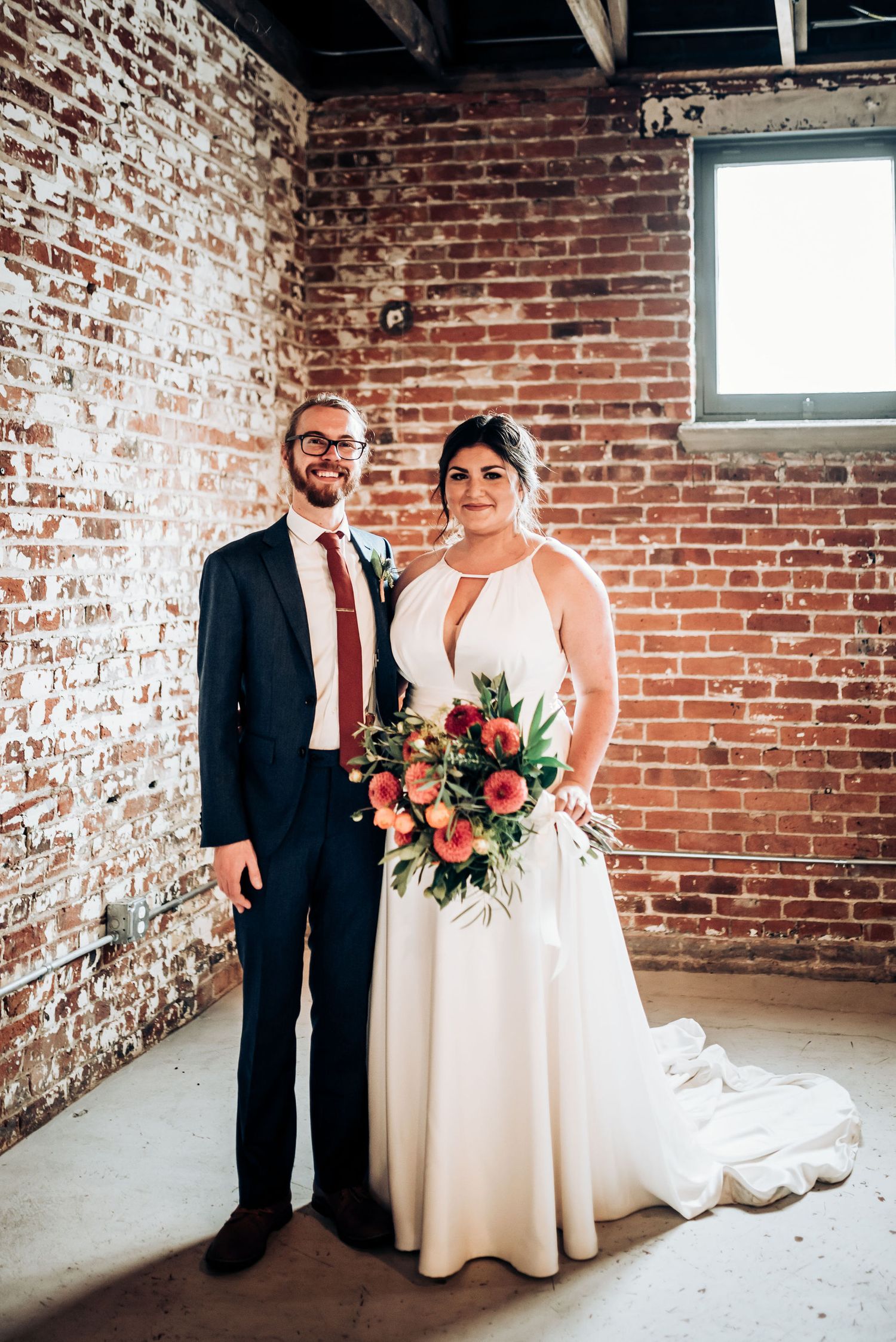 A wedding portrait in an industrial venue features a beautiful bouquet and elegant white gown.