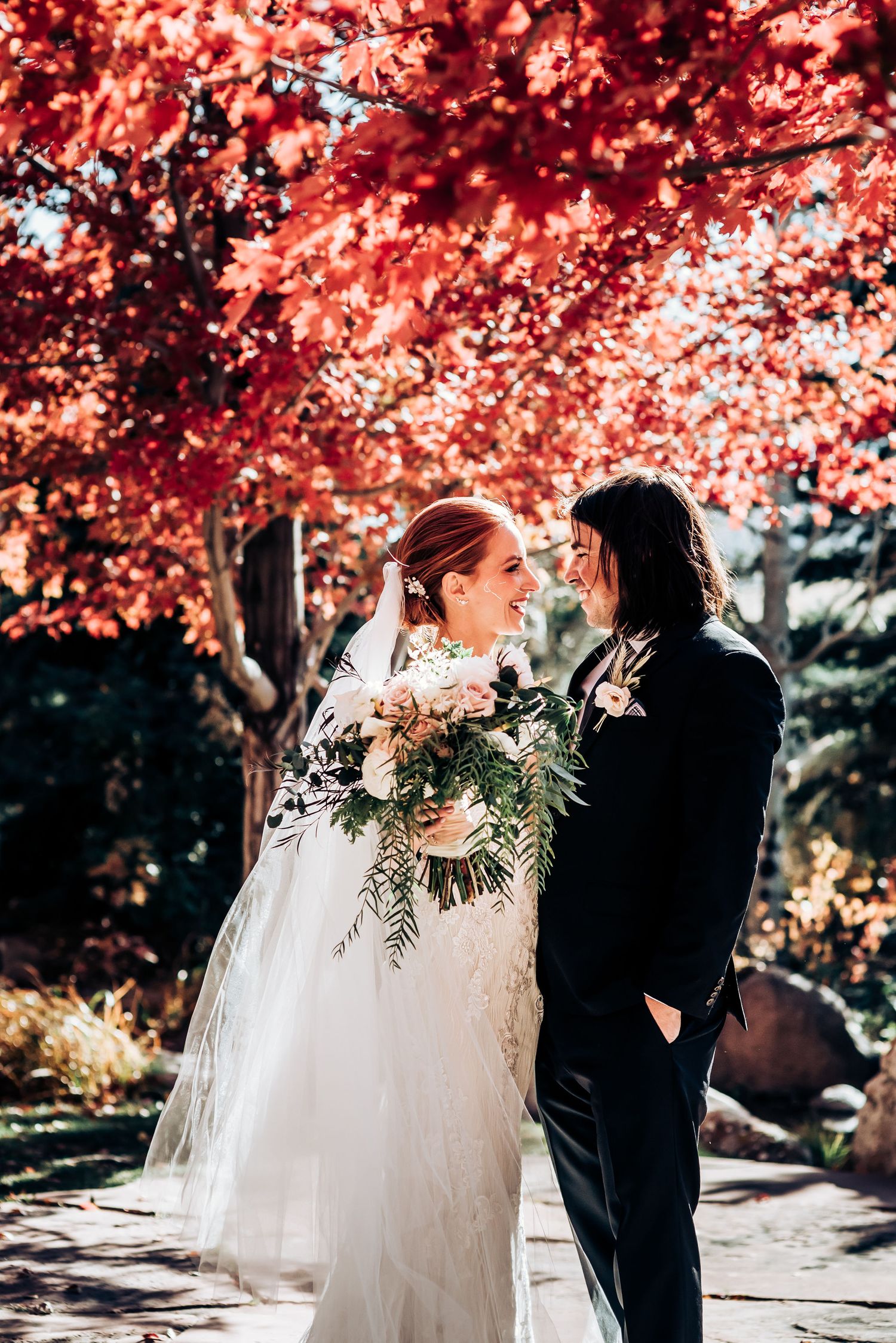 Newlyweds share an intimate moment beneath stunning red maple trees in a garden setting.