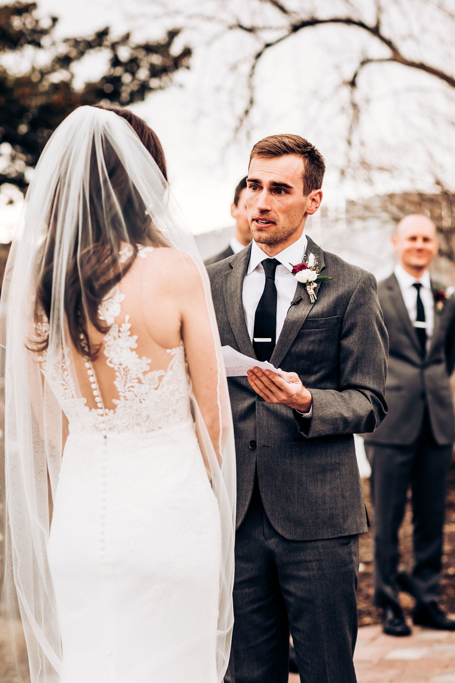 Wedding couple exchanging vows during outdoor ceremony with elegant formal attire.