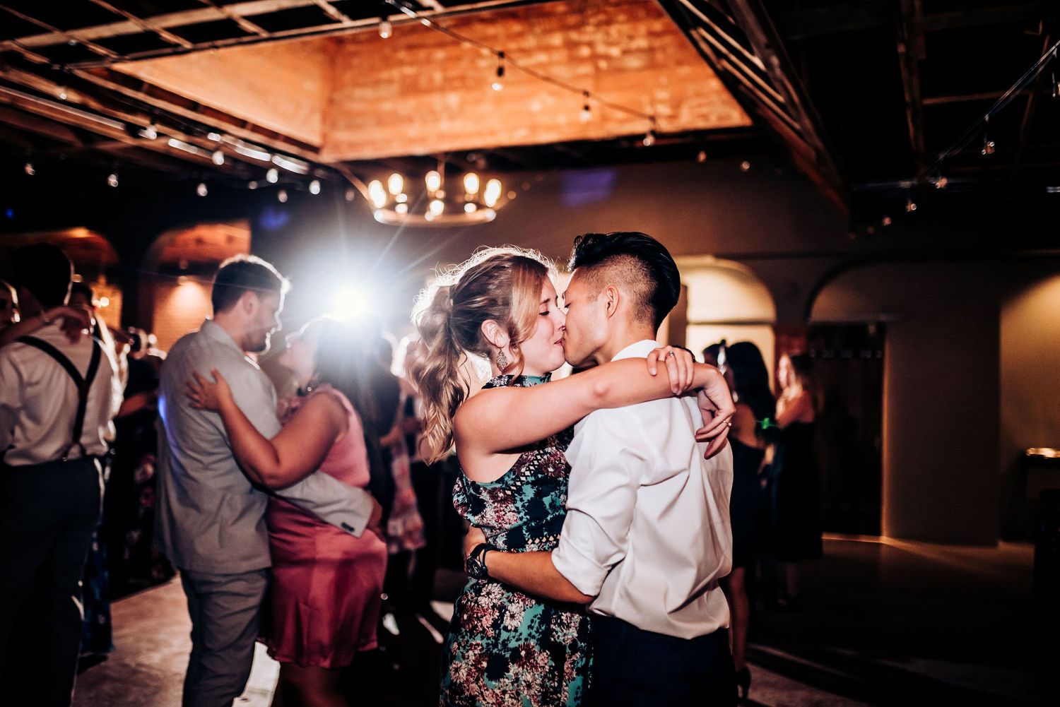 Couples dancing and celebrating at wedding reception with romantic lighting and brick walls.