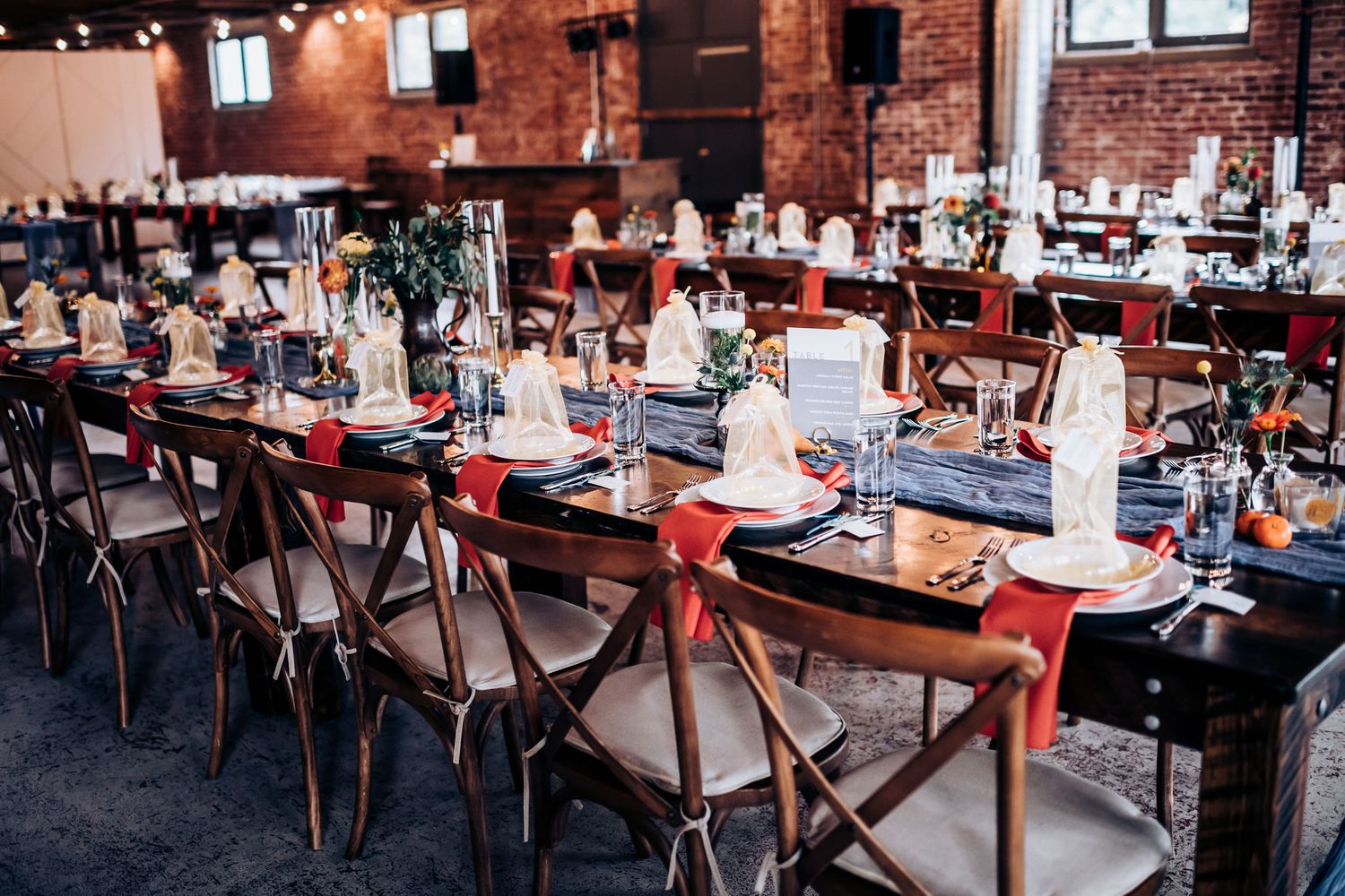 Rustic wedding reception setup with cross-back chairs and navy accents in brick-walled venue.