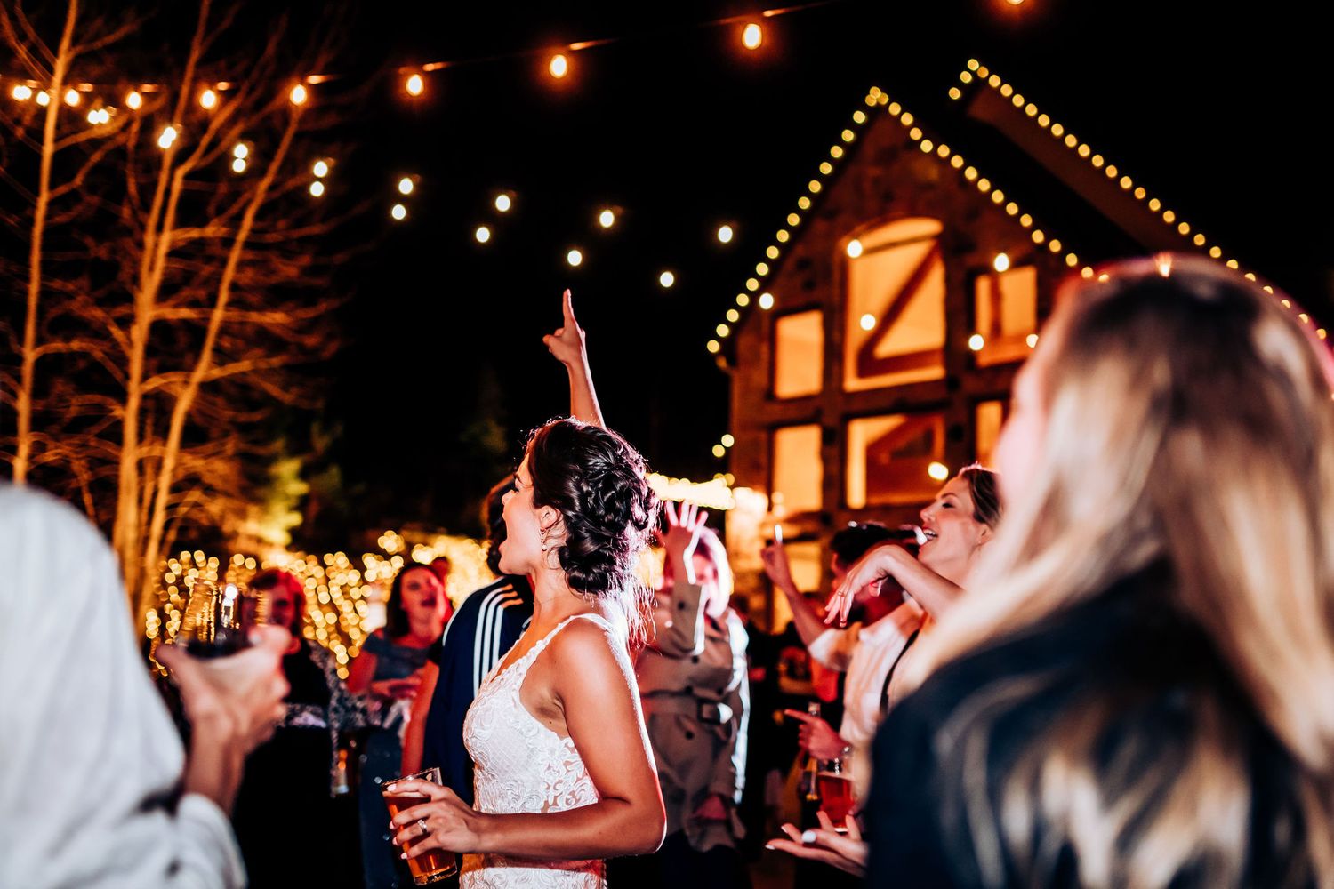 Festive outdoor wedding celebration with string lights and a rustic venue in the background.