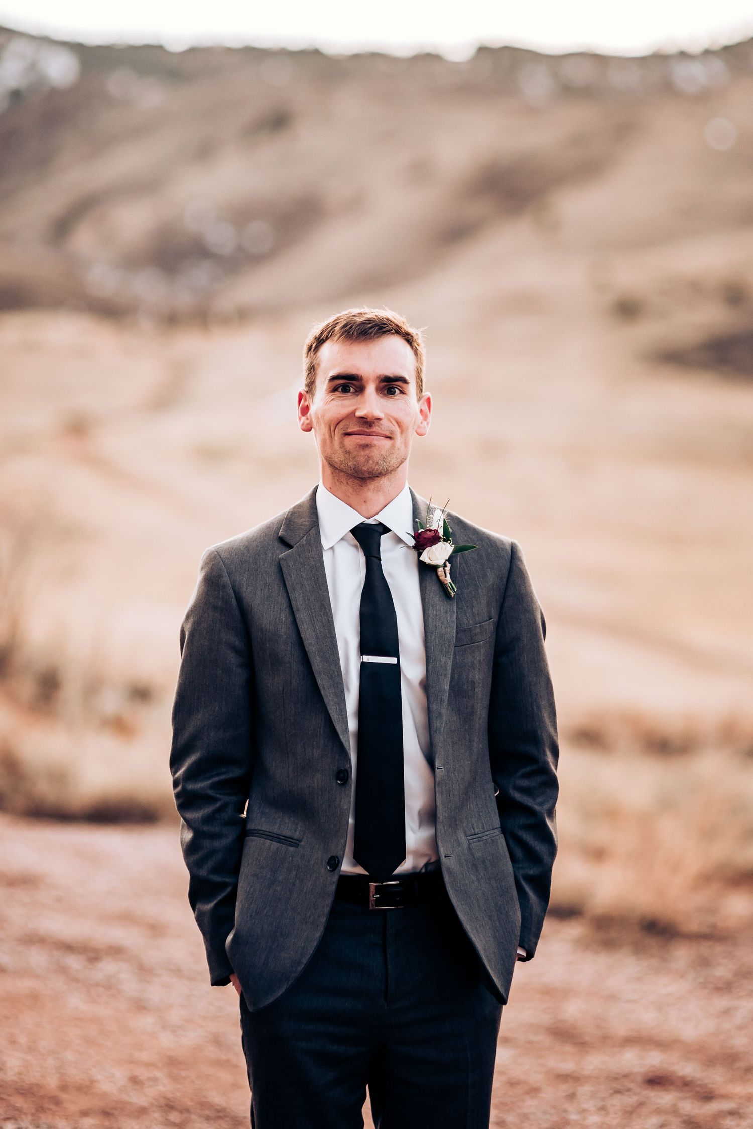 Groom in classic charcoal suit and tie poses against scenic mountain backdrop.