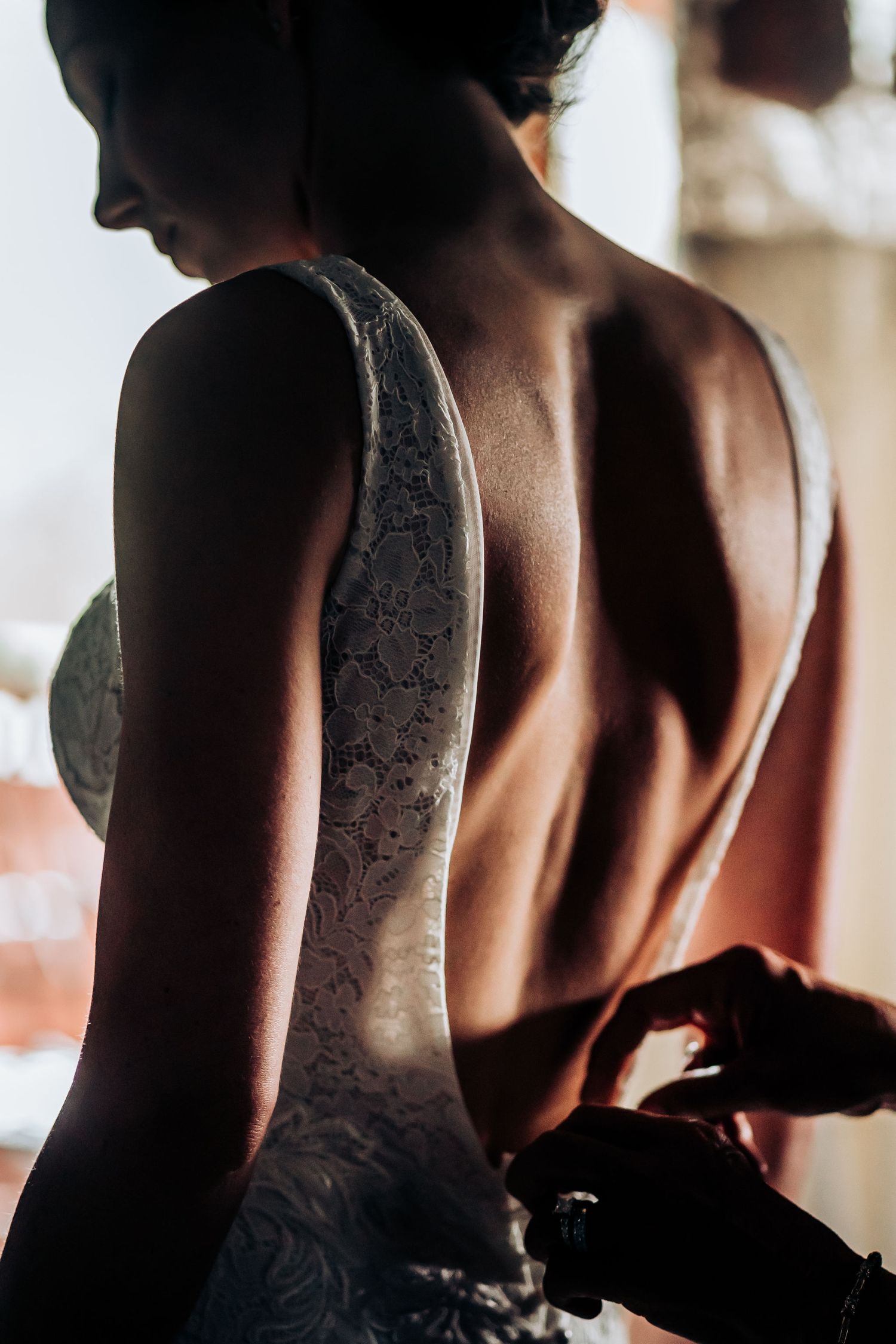 Detailed back of a white lace wedding dress shown in dramatic lighting.