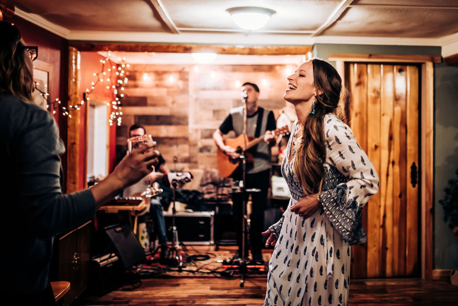Musicians perform on stage while woman in patterned dress sings in rustic venue.