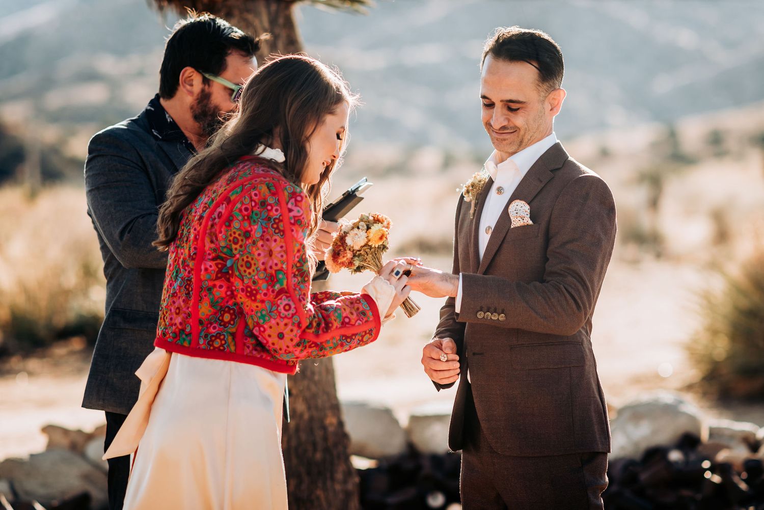 A couple celebrates during an outdoor desert wedding ceremony with guests watching in the background.