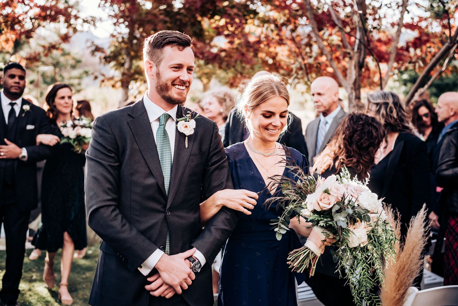 Wedding celebration against autumn trees with guests gathered to share joyful moments.