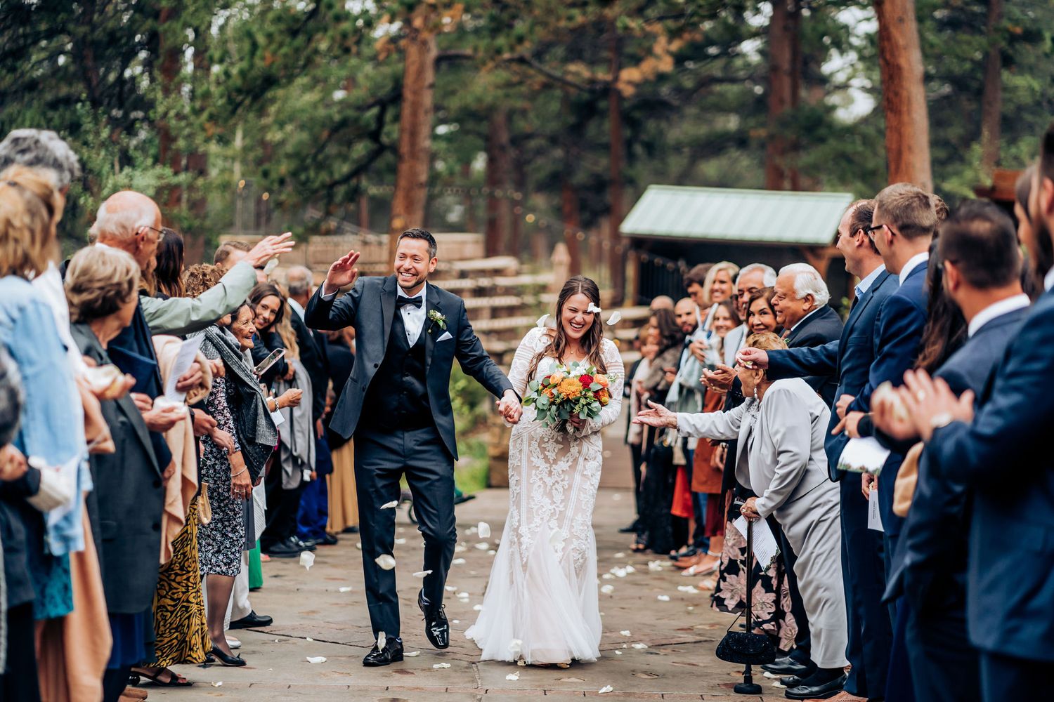Wedding guests line pathway throwing petals during newlywed couple's recessional walk.