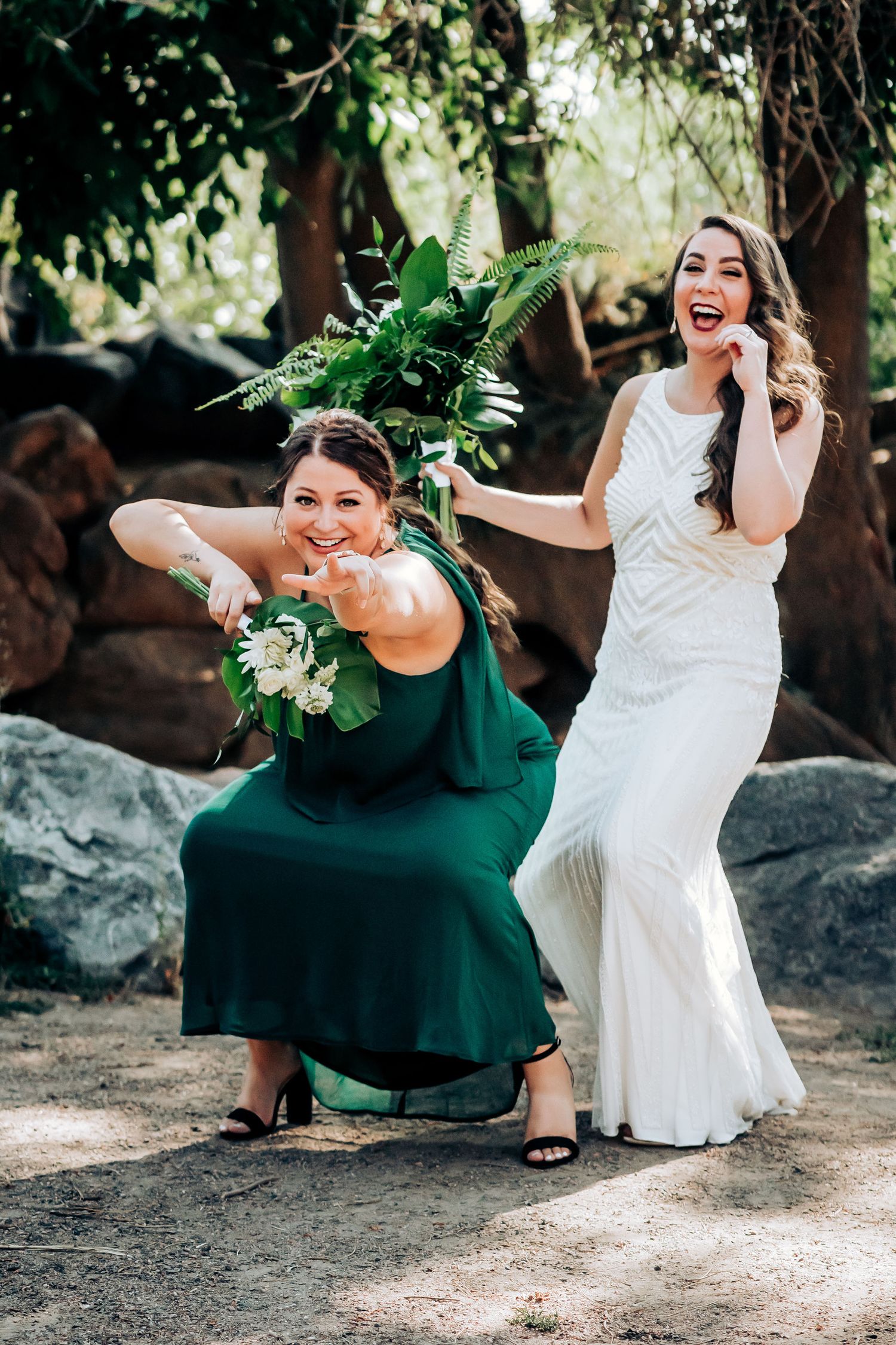 Wedding party members strike playful poses with tropical bouquets in an outdoor garden setting.