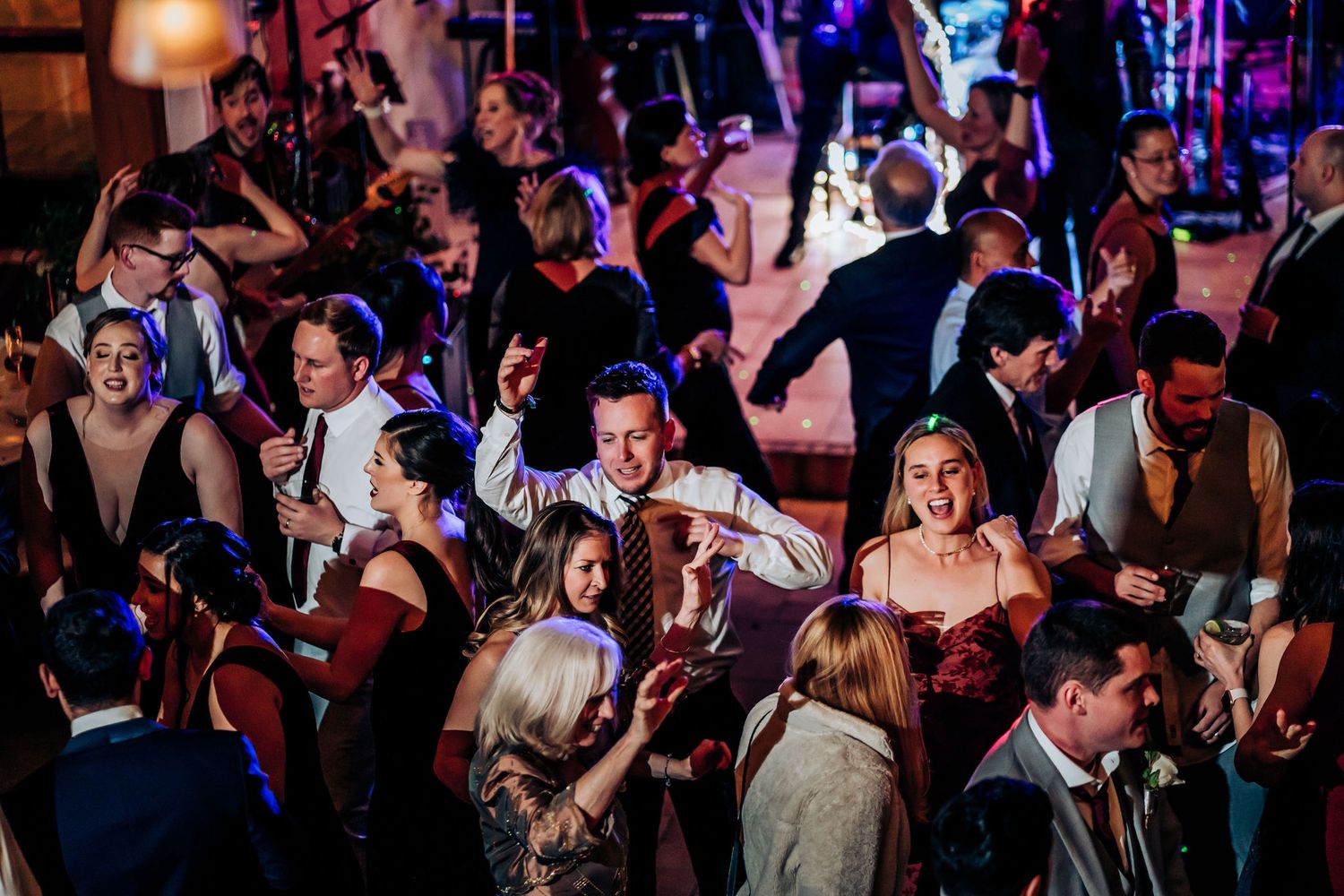 Energetic crowd dancing at a reception with colorful lighting effects.